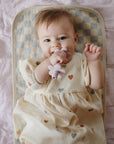 A baby chews a flower-shaped teether while lying on a Mushie Changing Pad Liner.