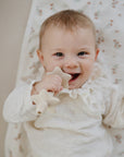 A happy baby on a Mushie Changing Pad Liner, chewing on a star-shaped teether.