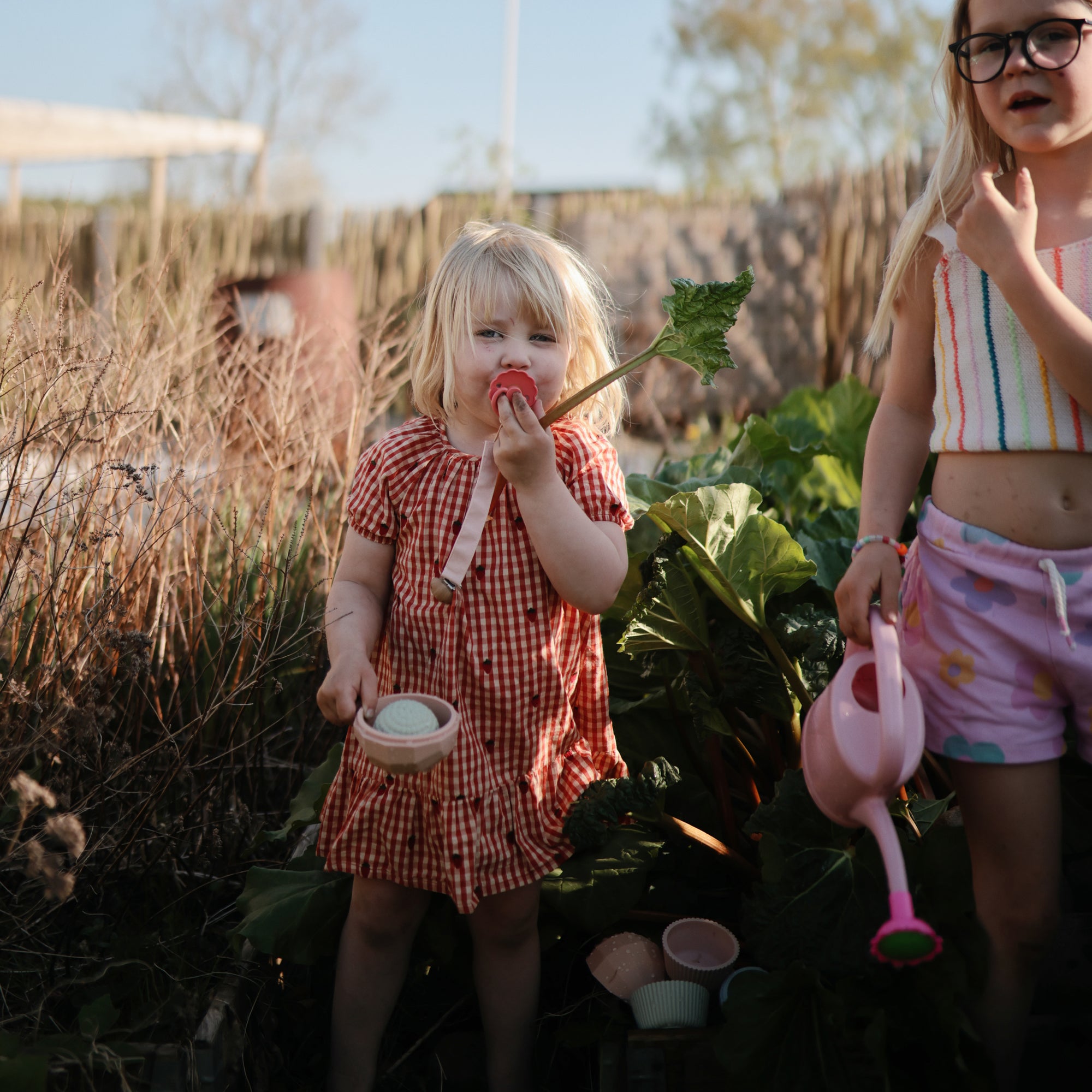 Two kids in a garden: one with a pink watering can, one with mushie's Nesting Spheres Sensory Toy.
