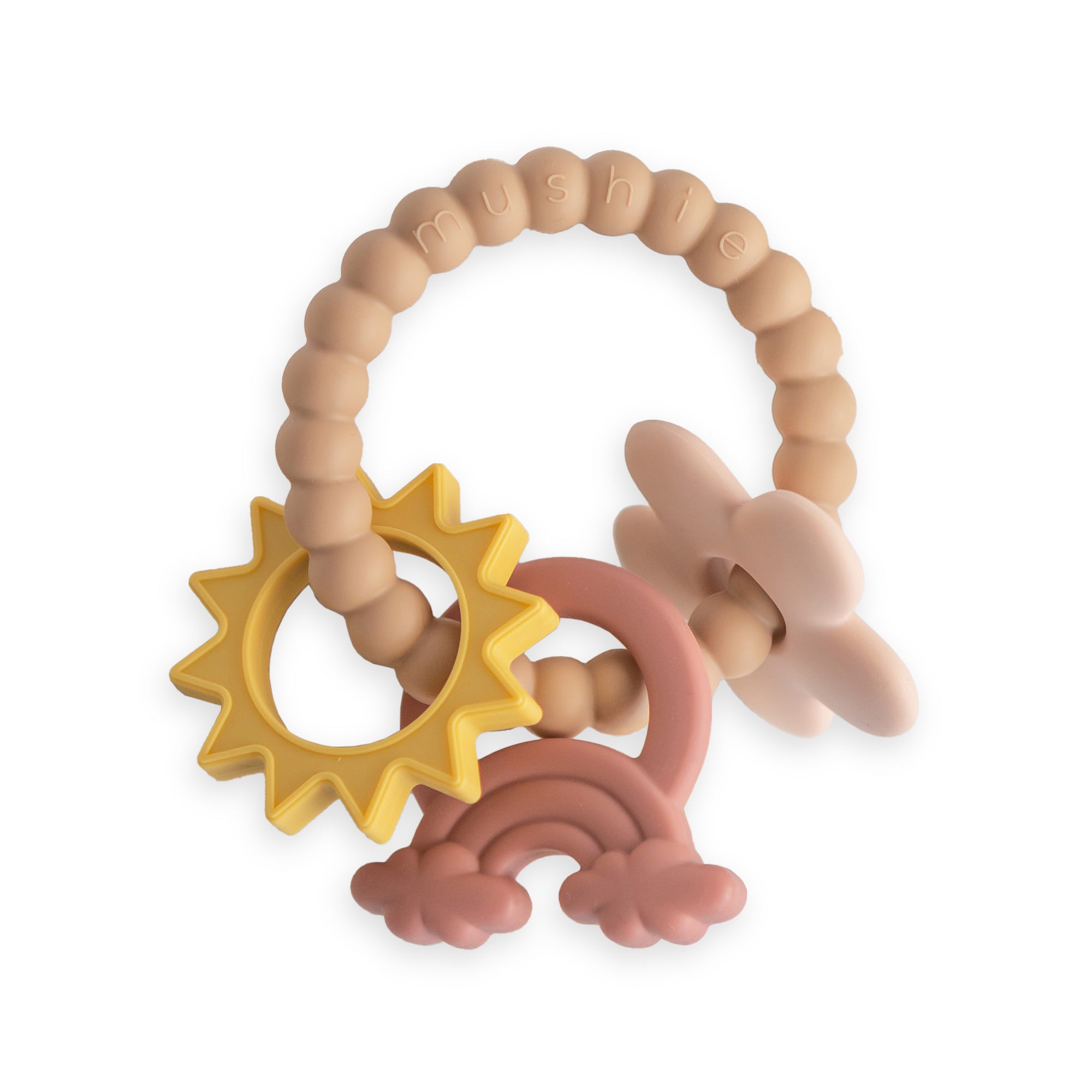 A silicone baby teether with soft beaded loops and attached shapes: a yellow sun, a pink and red rainbow, and a beige star. The brand name mushie is embossed on the loop.