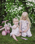 Two young girls on grass play with a mushie Silicone Sensory Toy, colored pencils nearby.