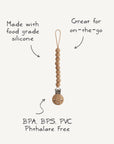 The mushie Silicone Pacifier Clip | Hera features a minimalist design with food-grade silicone beads and a wooden clasp. Free of BPA, BPS, PVC, and phthalates—ideal for on-the-go use.