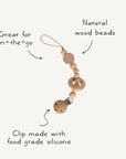 The mushie Silicone Pacifier Clip | Mila features natural wood beads, a circular wooden ring, and a food-grade silicone clip with looped string—combining safety and style for your little one’s on-the-go needs.
