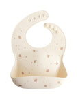 Mushie Silicone Baby Bib in cream with bird & star designs, adjustable neck strap.