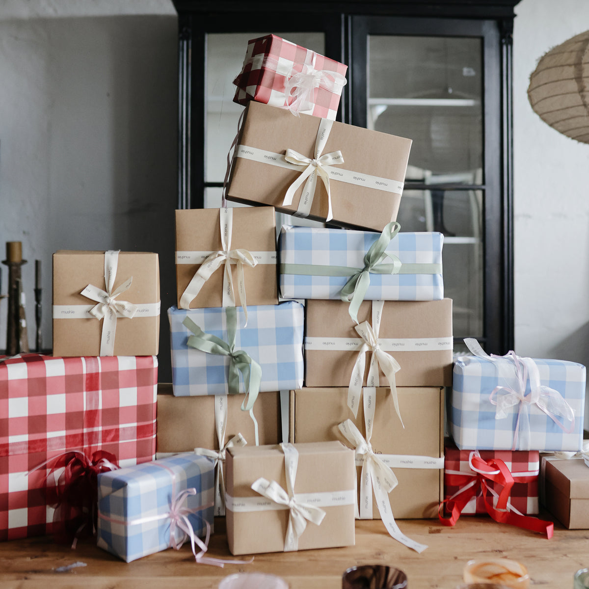 Playtime Gift Set by mushie sits on a wooden table in front of a cabinet, wrapped with ribbons.