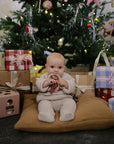 Baby enjoys mushie Playtime Gift Set by the tree, surrounded by gifts and sensory toys.