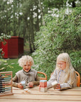 Two children play with mushie Mix and Match Toy at a wooden outdoor table.
