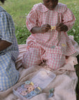 Two children play on a mushie Organic Cotton Muslin Swaddle Blanket with flower-shaped beads.