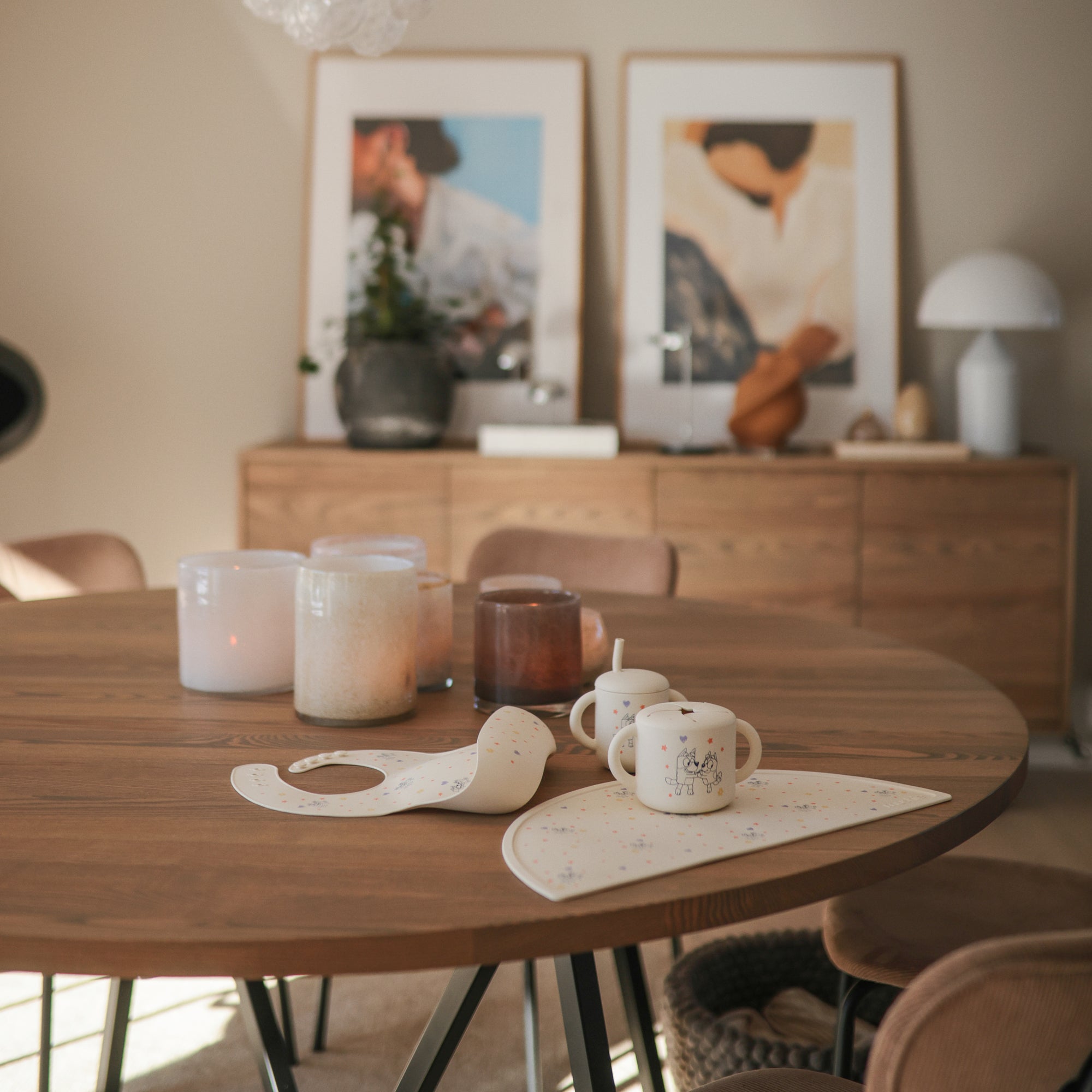 A wooden table with the Bluey Gift Set by mushie, candles, mugs, and art in the background.