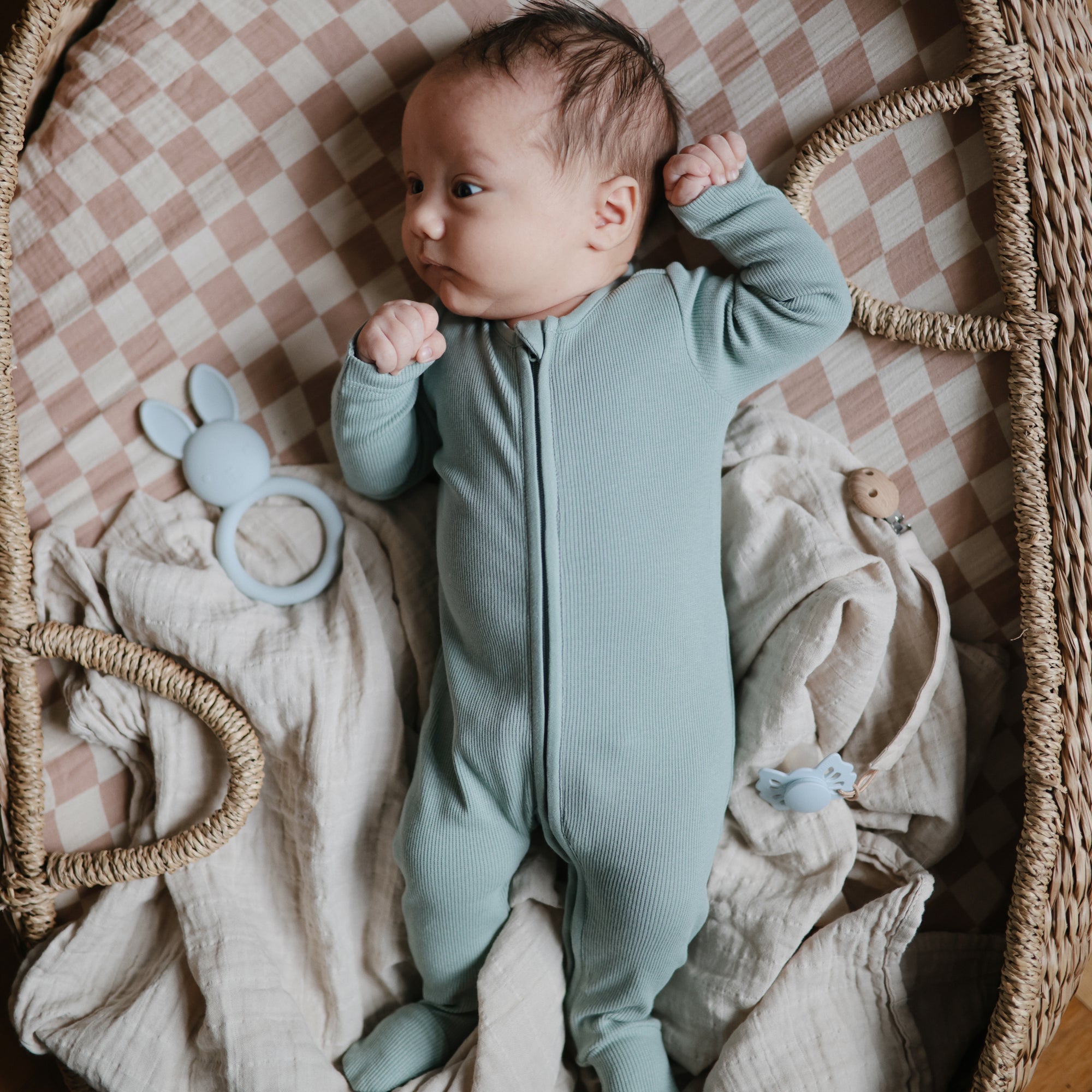 Baby in a light blue onesie with toys and a mushie Organic Cotton Muslin Swaddle Blanket.