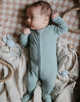 Baby in a light blue onesie with toys and a mushie Organic Cotton Muslin Swaddle Blanket.