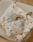 A space-patterned fabric pouch with zippers rests on a beige chair. Inside are a folded cloth and the mushie Bear Teether, a non-toxic accessory ideal for soothing little gums.