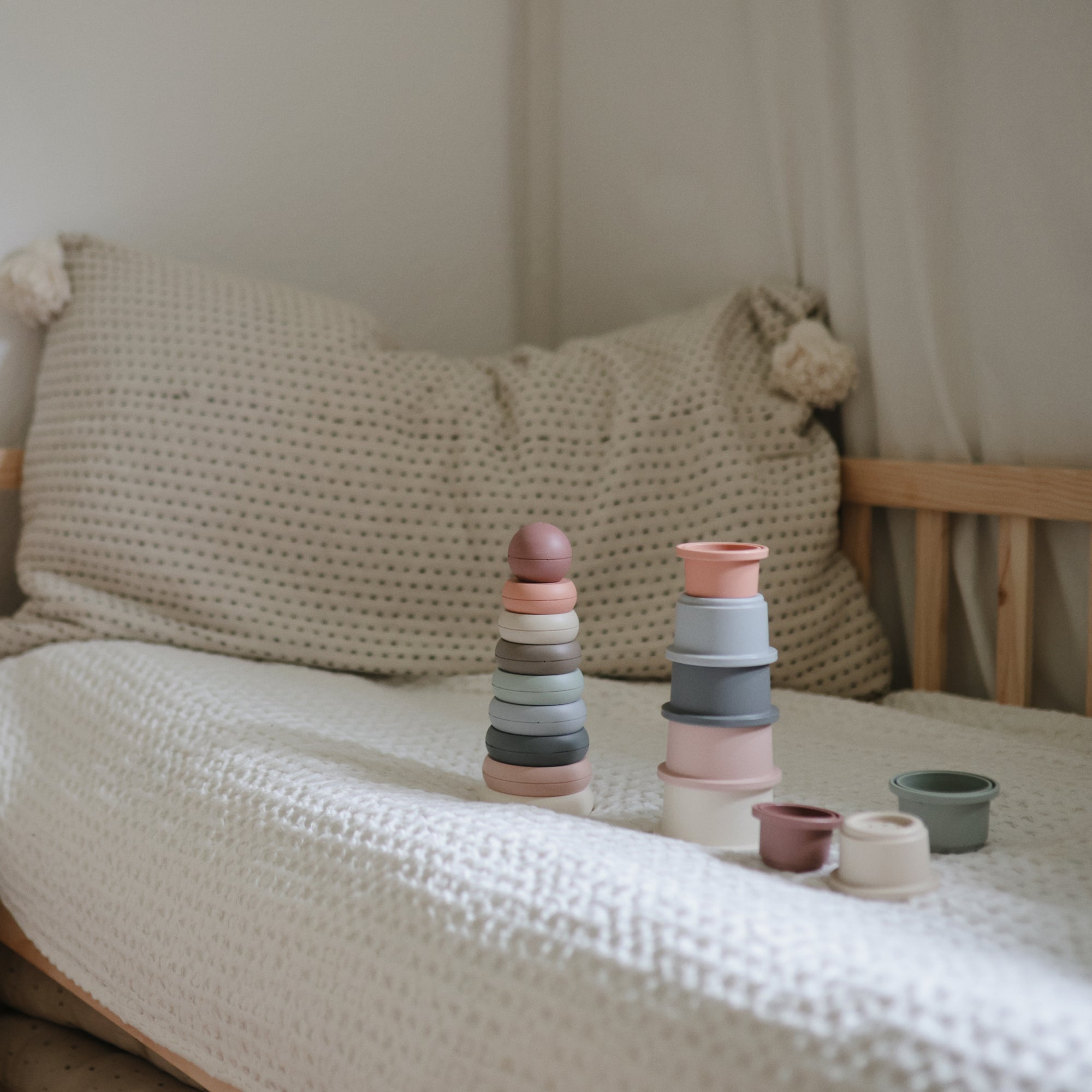 Two mushie Stacking Cups Toys on a bed, perfect for building baby motor skills and cozy play.