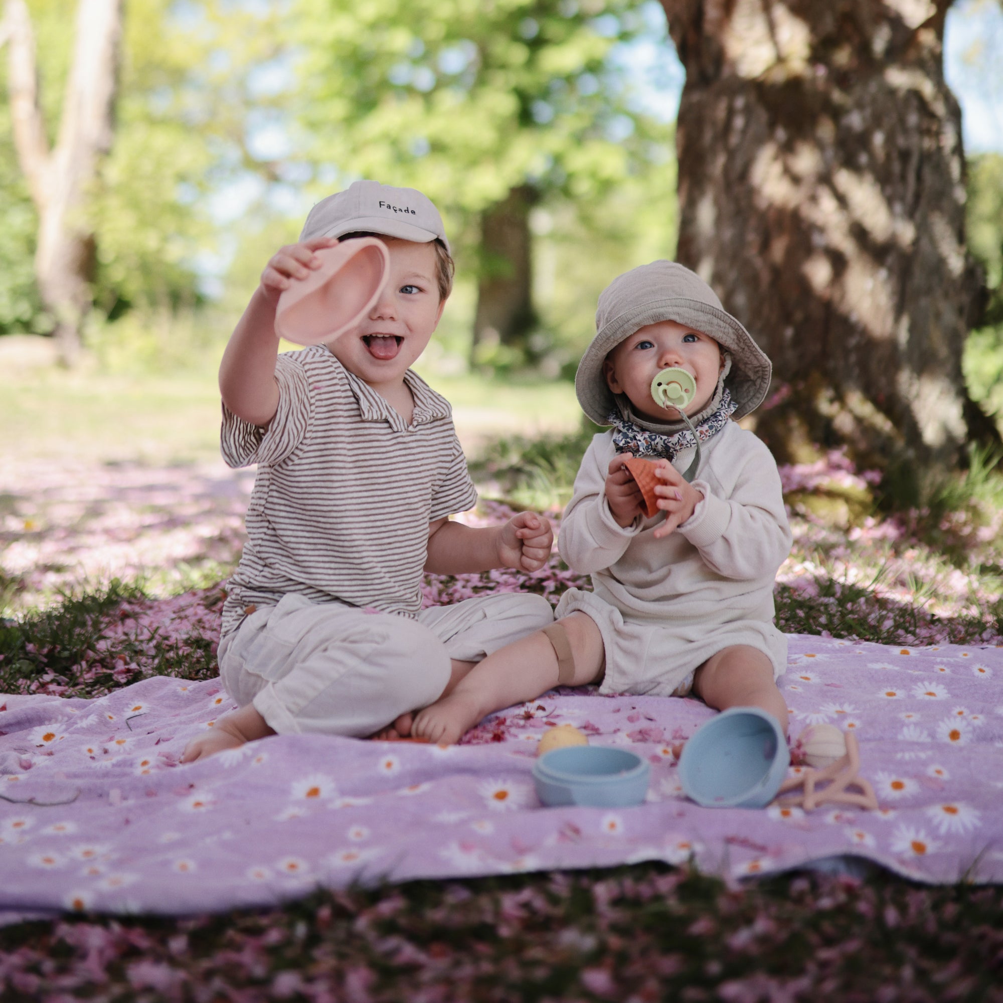 Two kids enjoy a sunny picnic with the mushie Nesting Spheres Sensory Toy on a blanket.