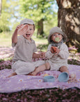 Two kids enjoy a sunny picnic with the mushie Nesting Spheres Sensory Toy on a blanket.
