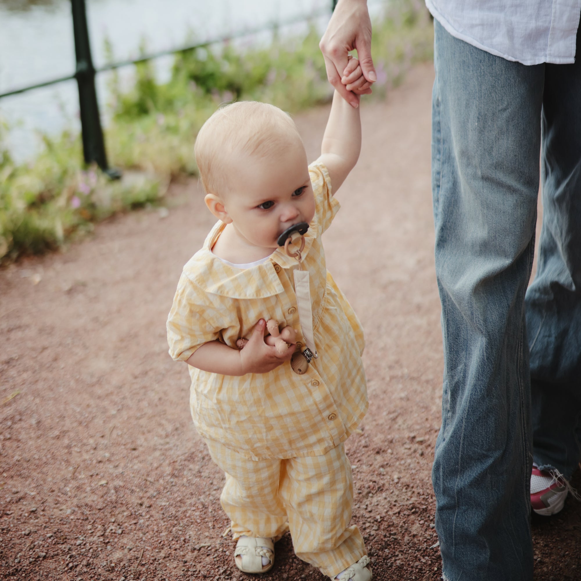 A toddler in yellow walks outside, sucking a FRIGG Daisy Natural Rubber Pacifier.