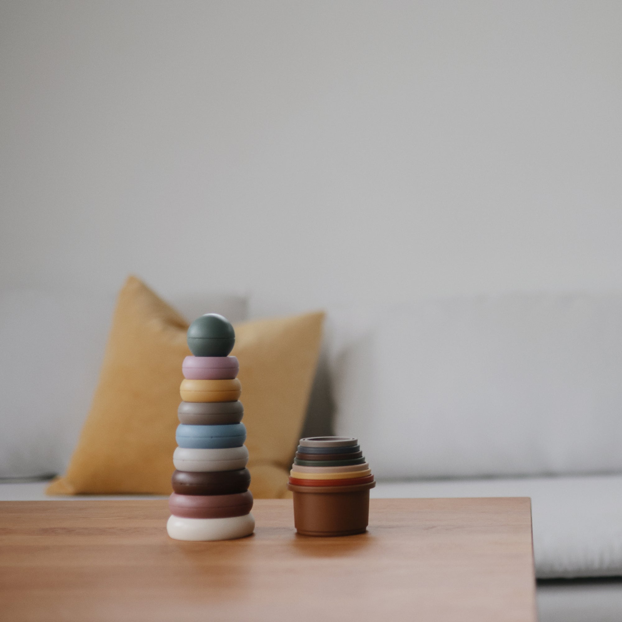 Mushie Stacking Cups Toy on a table, with a sofa and yellow pillow in the background.