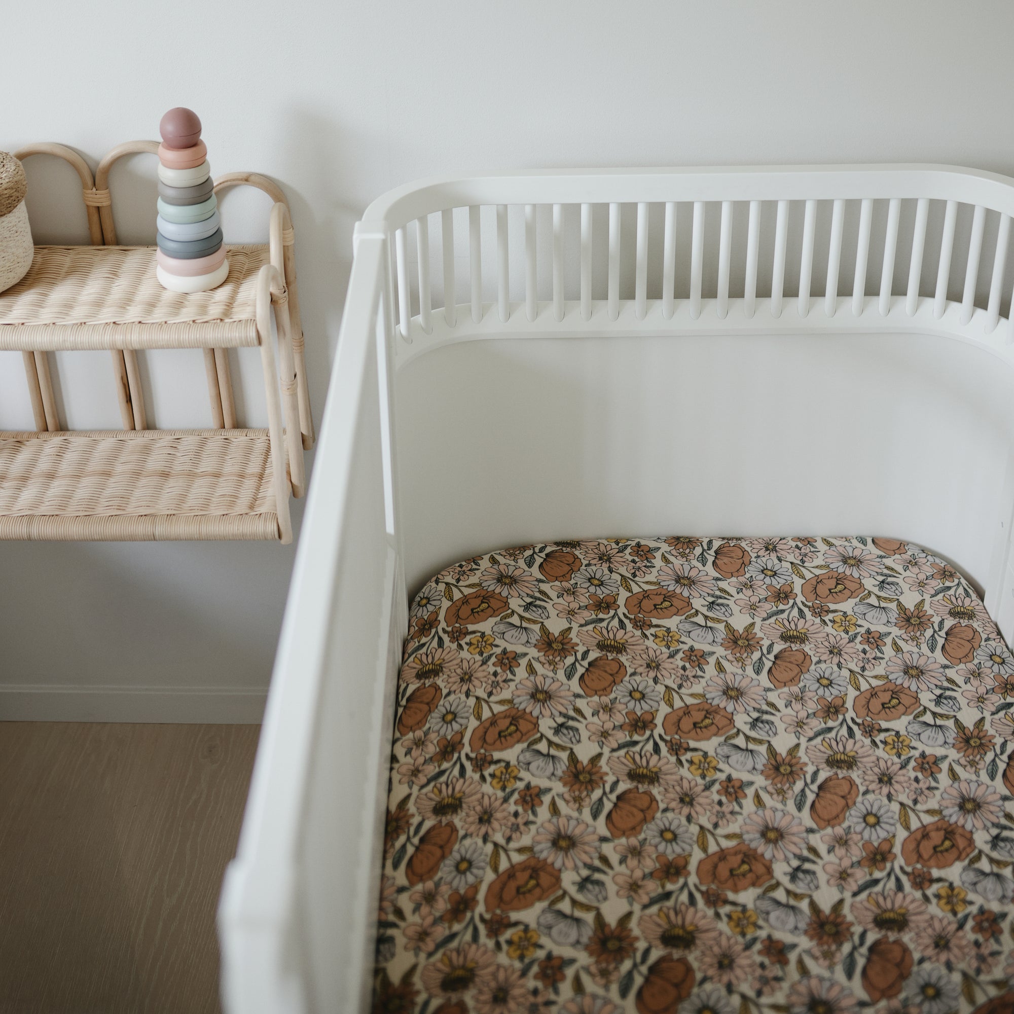White crib with mushie Extra Soft Muslin Crib Sheet beside a shelf with stacking toy and basket.