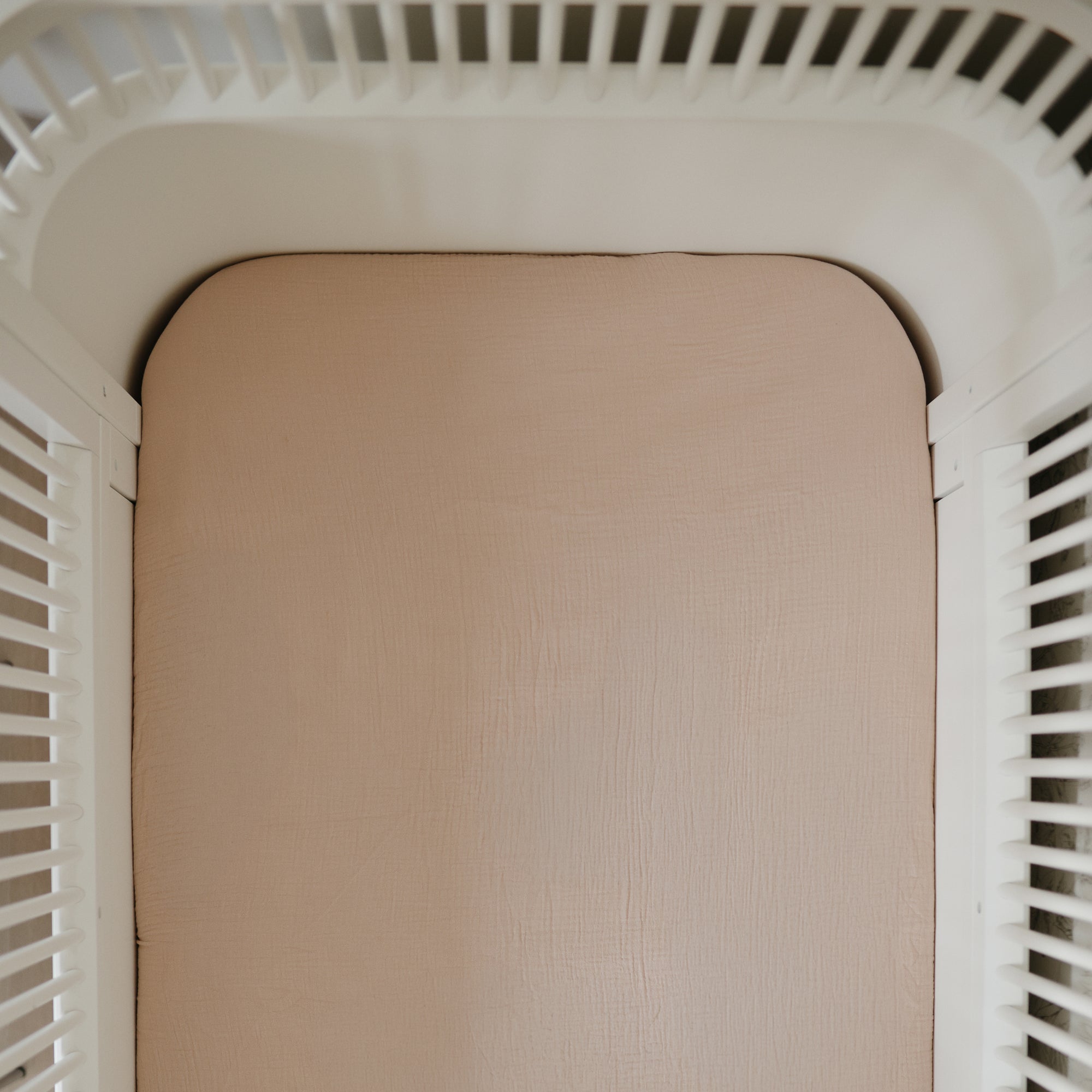 Mushie Extra Soft Muslin Crib Sheet on beige mattress in white slatted crib, top view.