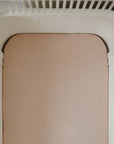 Mushie Extra Soft Muslin Crib Sheet on beige mattress in white slatted crib, top view.