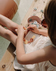 Child in white dress playing with mushie HEX Connect Building Toy Set, boosting spatial skills.