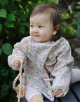 Happy baby outside in a floral mushie Long Sleeve Bib, holding a beaded toy.