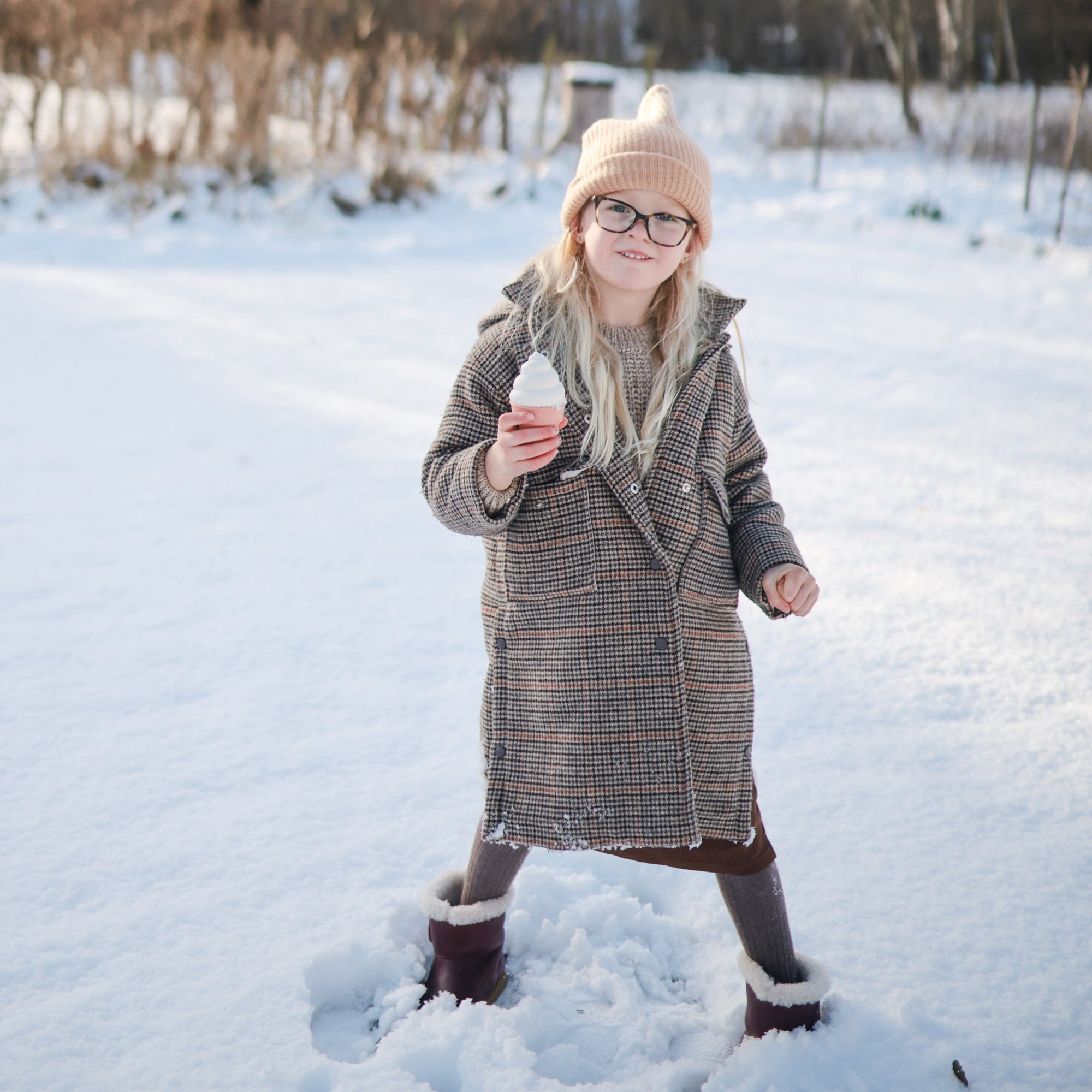Girl plays with mushie Mix and Match Toy outside in snow, practicing fine motor skills.