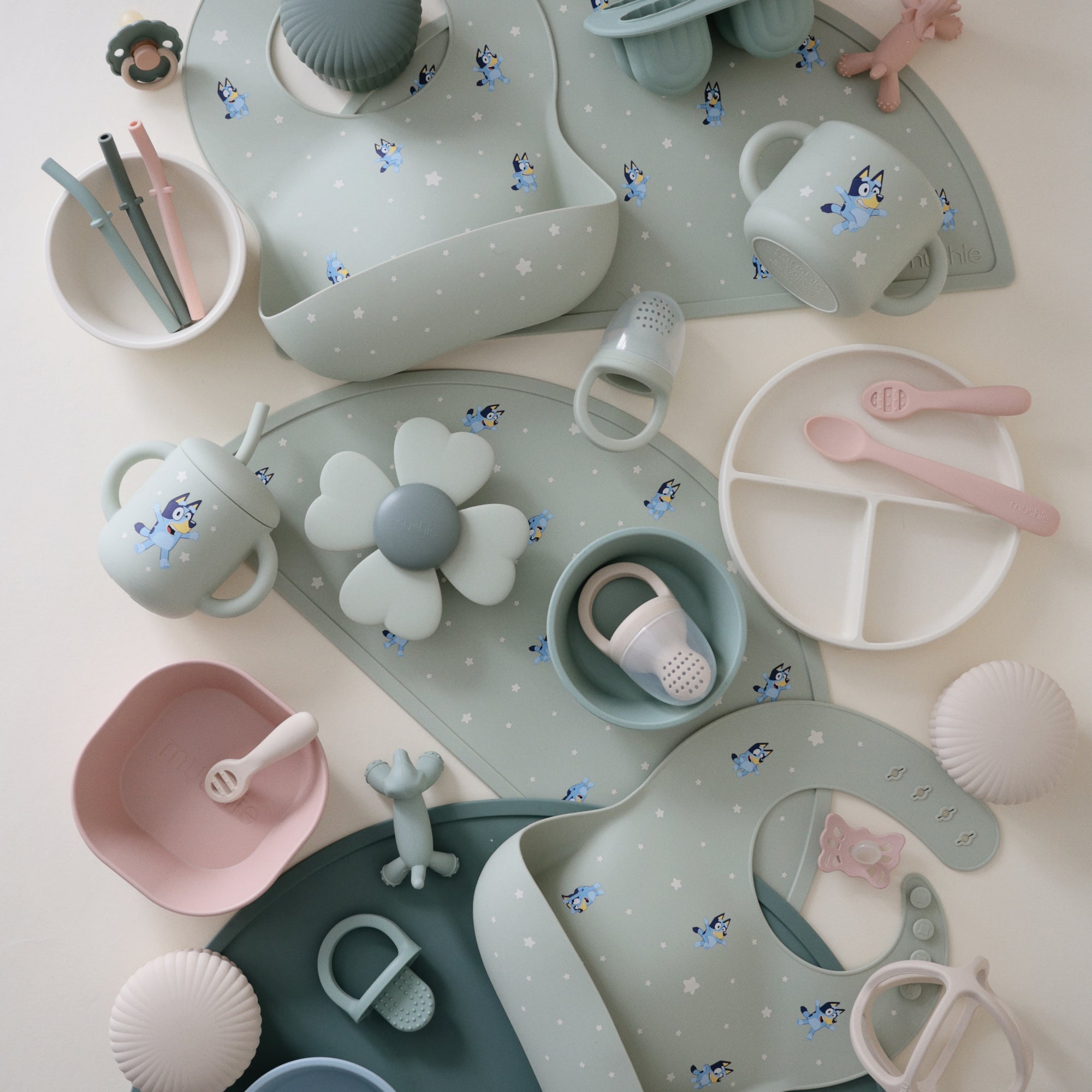 Mushie Bluey Gift Set: pastel silicone baby feeding items and toys with themed bibs displayed.
