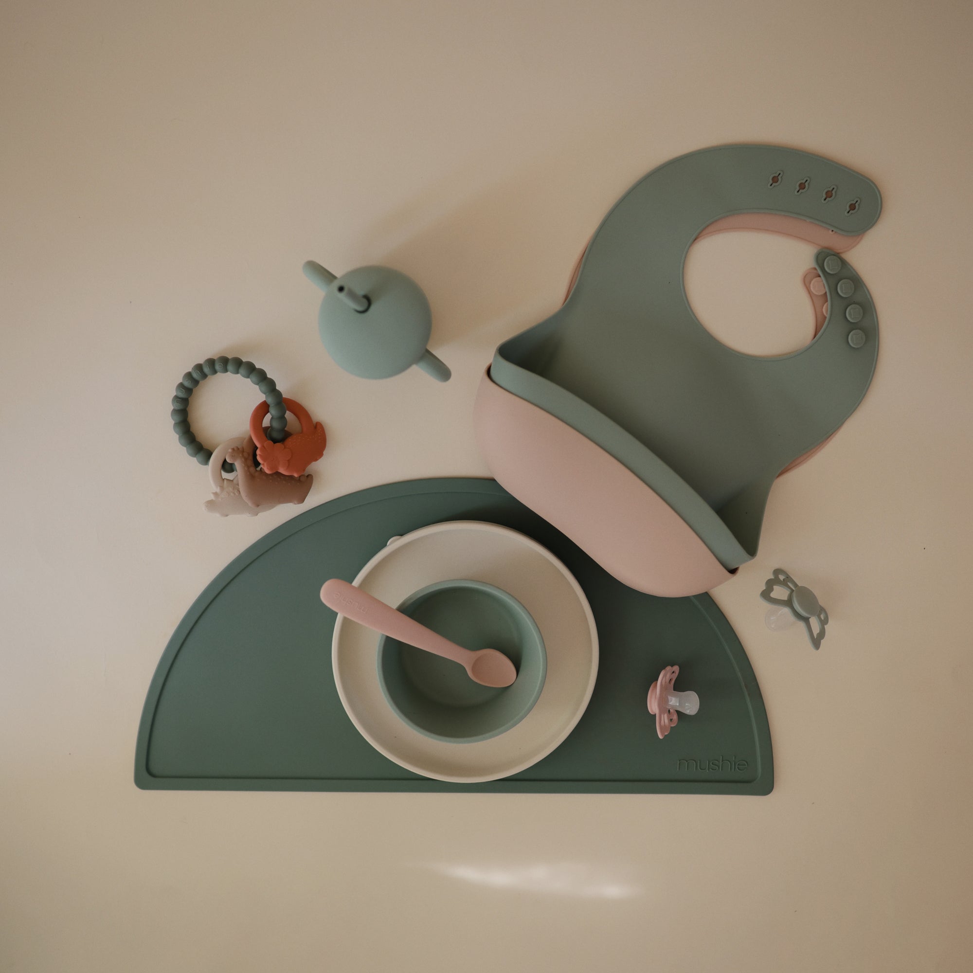Mushie Teething Ring set: food-grade silicone ring, bowl, cup, spoon, bib, and mat.