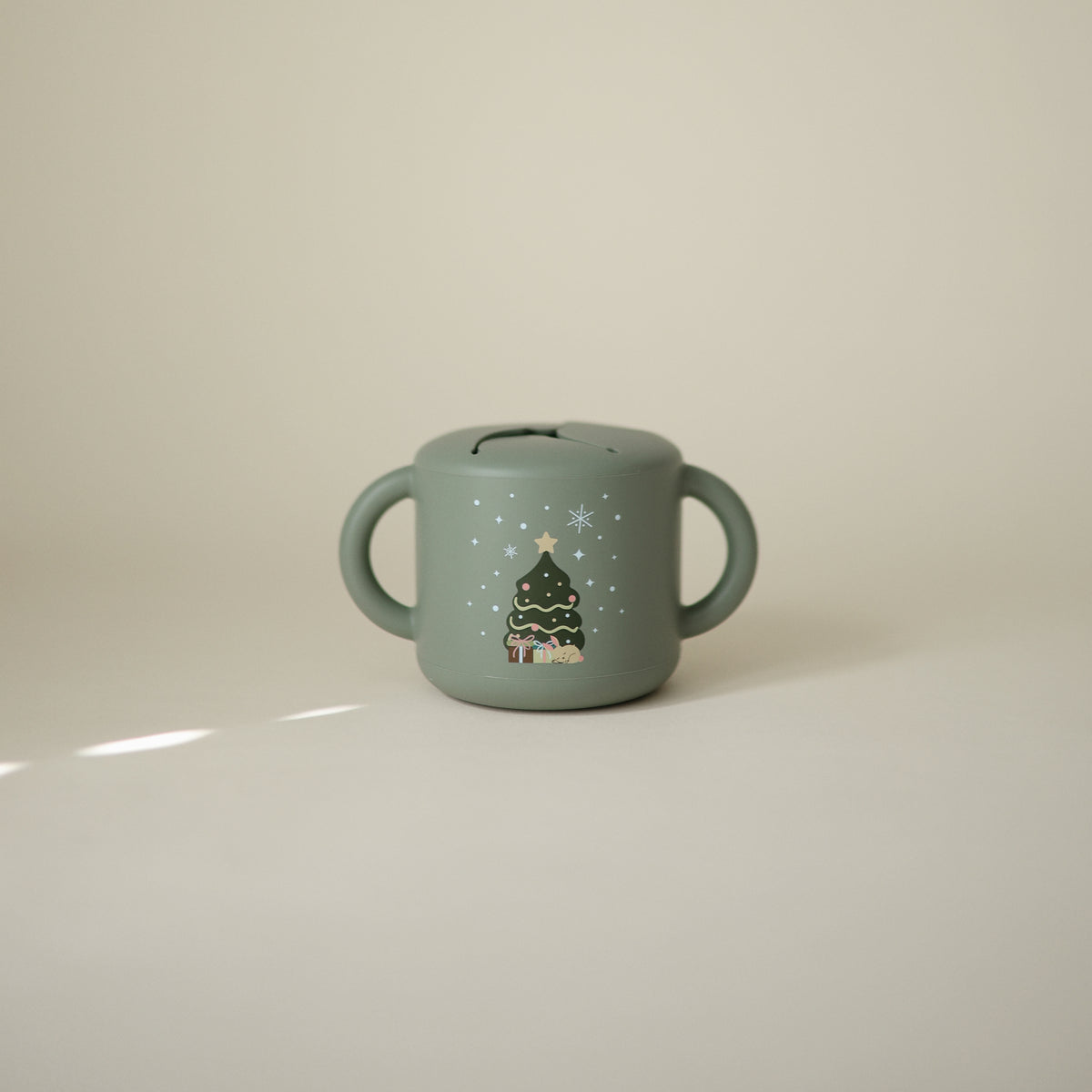 Mushie Snack Cup—green, spill-proof, handles, Christmas tree design; ideal for toddlers.