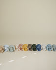 Five FRIGG Rope Natural Rubber Pacifier 2-Packs by Mushie arranged on a neutral background.
