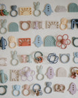 Mushie Figurine Teether toys in assorted pastels displayed on a white background.