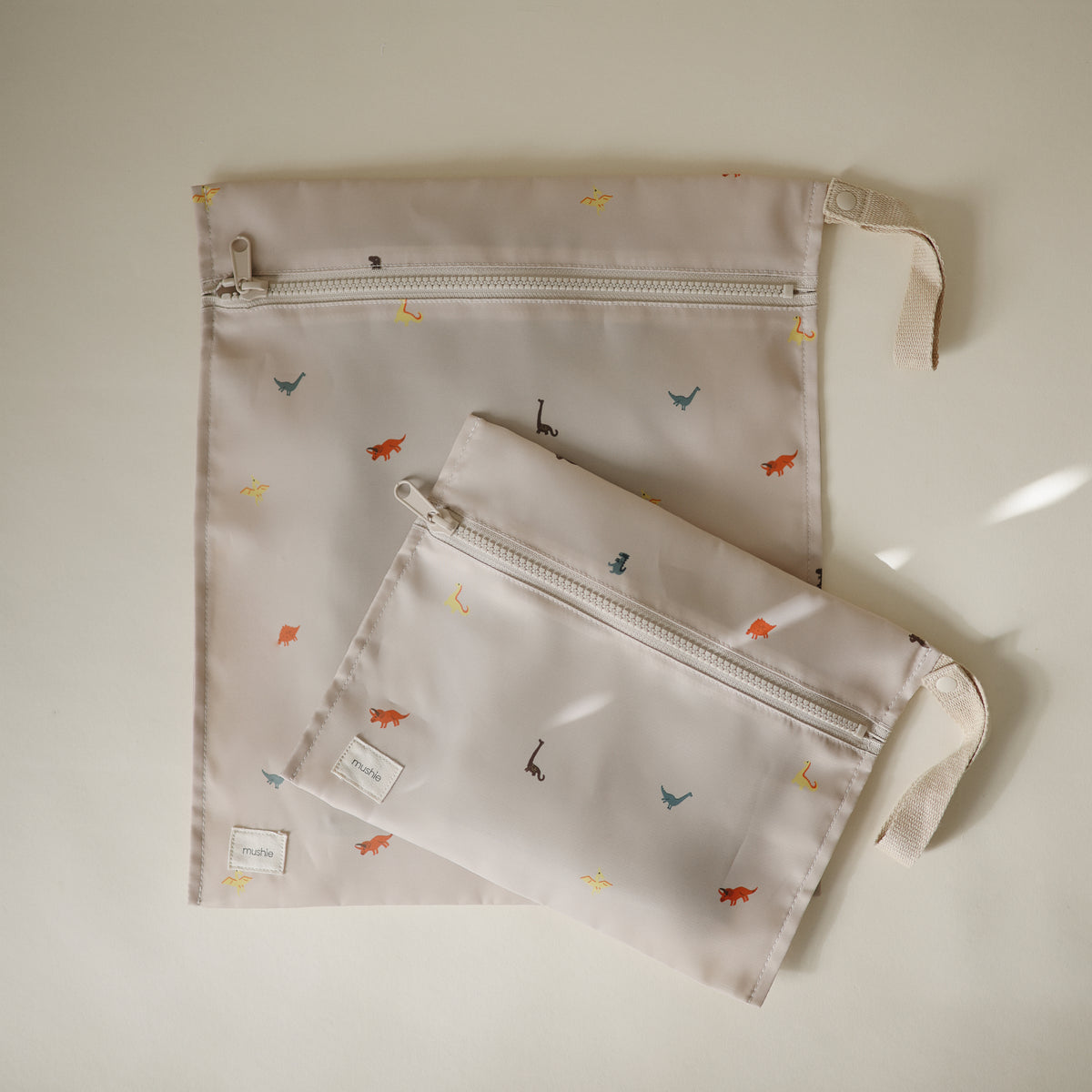 Two beige Water Resistant Wet Bag pouches with zippered closures and dinosaur illustrations.