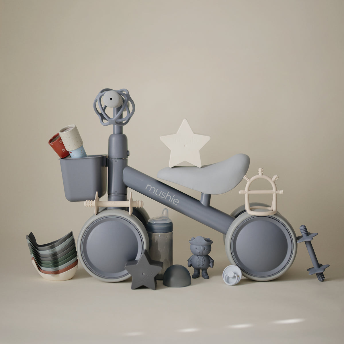 A mushie Mini Toddler Bike surrounded by baby toys and accessories.