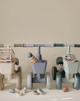 Three beige, blue, and sage green mushie Mini Toddler bikes, each with a front basket and toy.