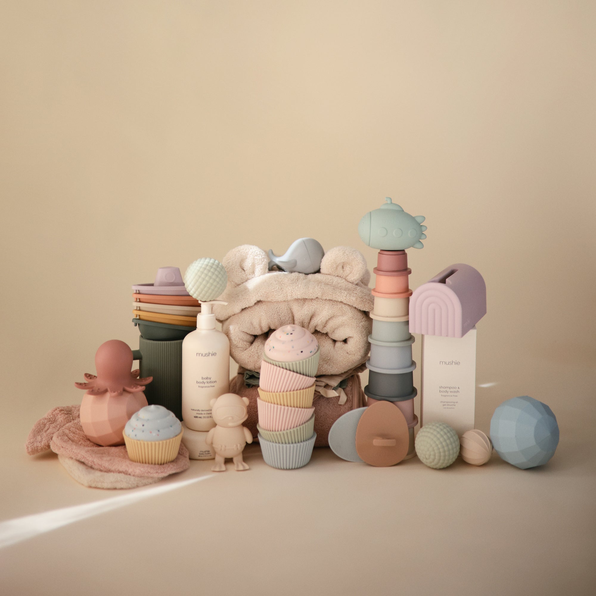 Mushie Mix and Match Toy softly arranged on beige with silicone cupcakes and a hooded towel.