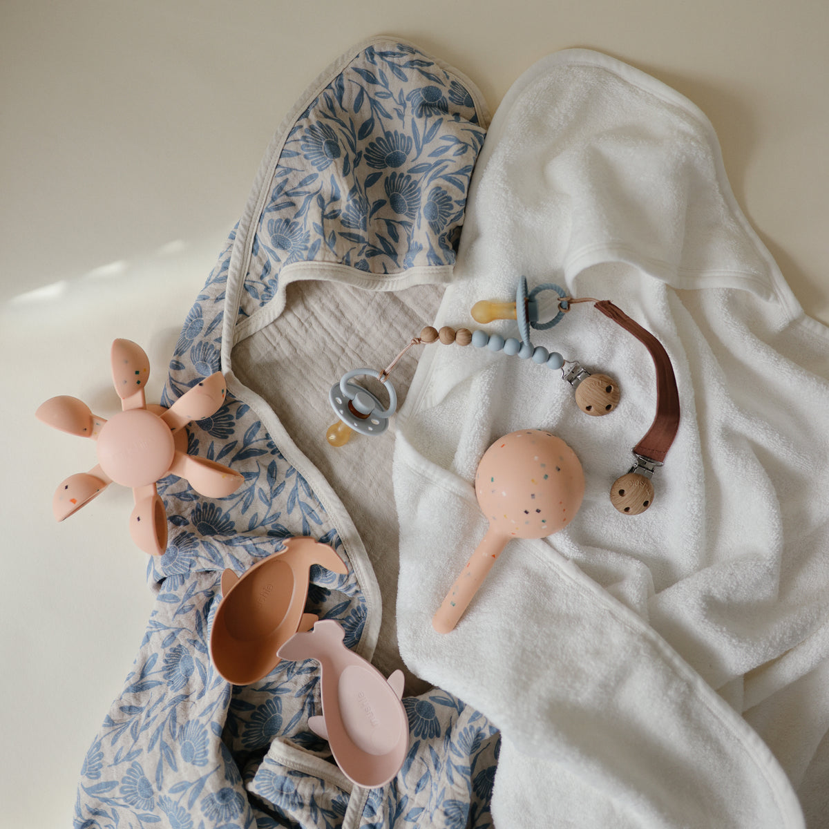 Baby items: floral hooded towel, pacifiers w/clips, and mushie Water Wheel Bath Toy in fun colors.
