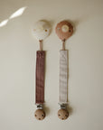 Mushie Linen Pacifier Clip 2-Pack with wooden clasps, includes one brown and one beige.