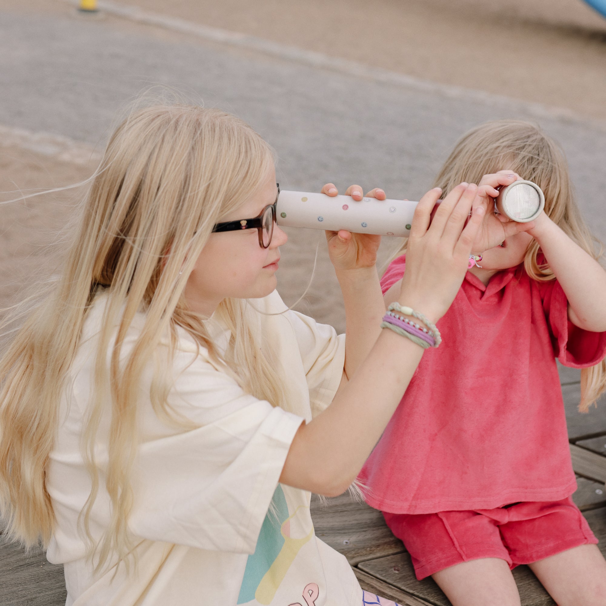 Two kids play outside, peering through mushie Kaleidoscopes.
