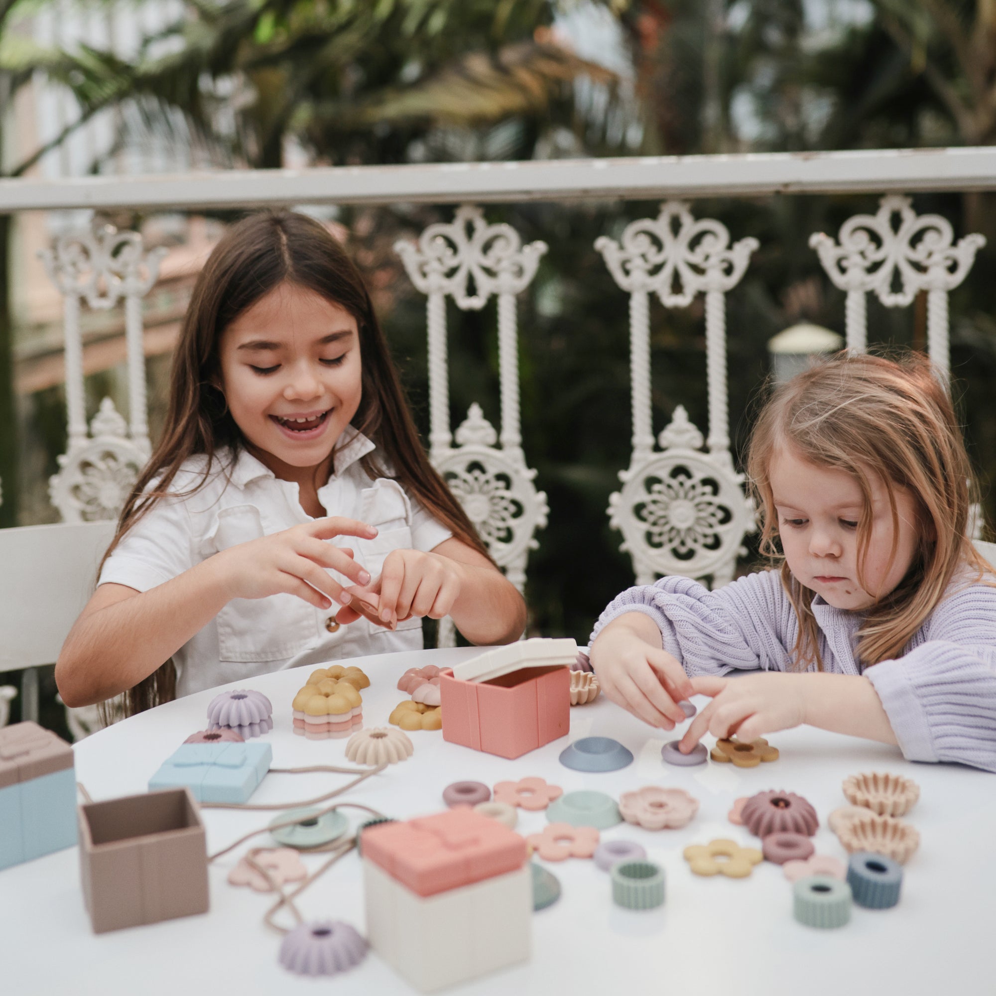 Two young girls build fine motor skills with the mushie Bead Lacing Toy Set.