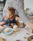 Toddler eats pastry from Mushie Classic Silicone Suction Plate; adult helps another child nearby.