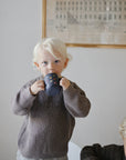 Blonde toddler in brown sweater drinks from Mushie Silicone Training Cup + Straw indoors.