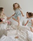 Woman holds baby as two girls jump on bed near a mushie Diaper Caddy.