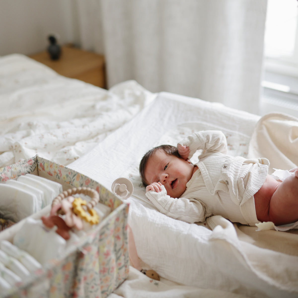 Newborn on bed beside a mushie Diaper Caddy, filled with baby essentials.