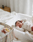 Newborn on bed beside a mushie Diaper Caddy, filled with baby essentials.