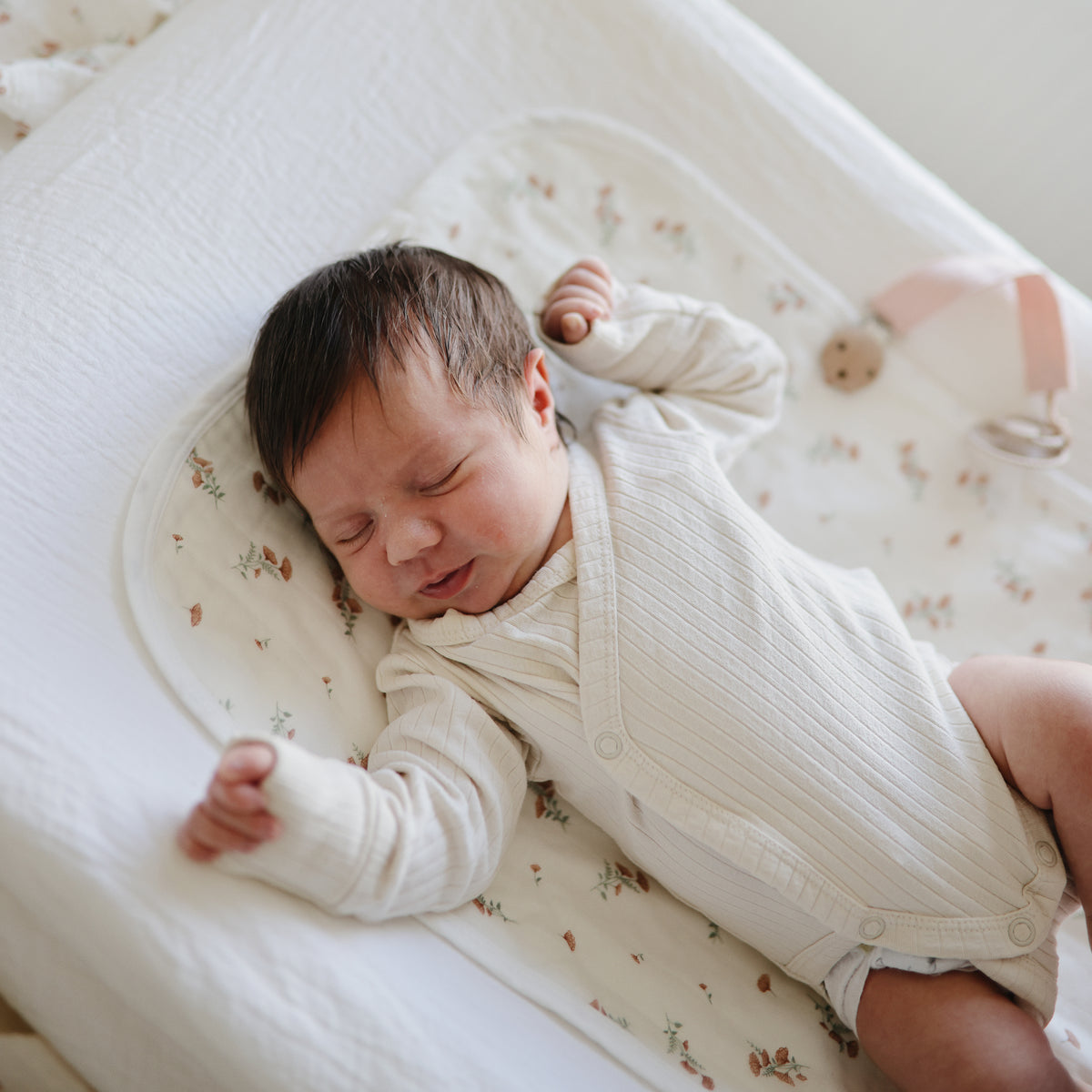 Newborn on patterned blanket with Mushie Changing Pad Liners, eyes closed, arms stretched.
