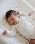 Newborn on patterned blanket with Mushie Changing Pad Liners, eyes closed, arms stretched.