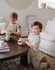 Two young children play with a mushie Nesting Spheres Sensory Toy on a coffee table.