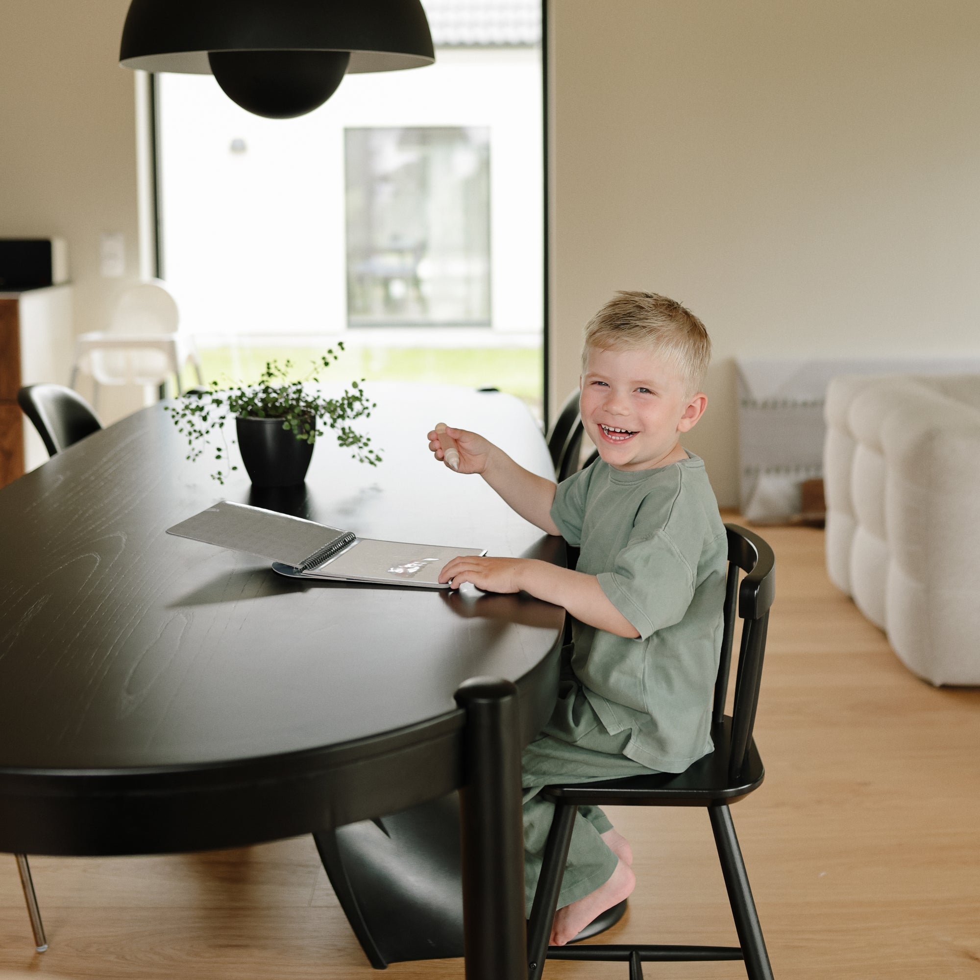 Smiling child at a black table using mushie's Reusable Water Color Pad.