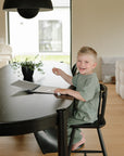 Smiling child at a black table using mushie's Reusable Water Color Pad.